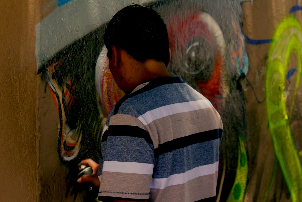 An artist, seen from behind, spray-painting a colorful mural on a wall.