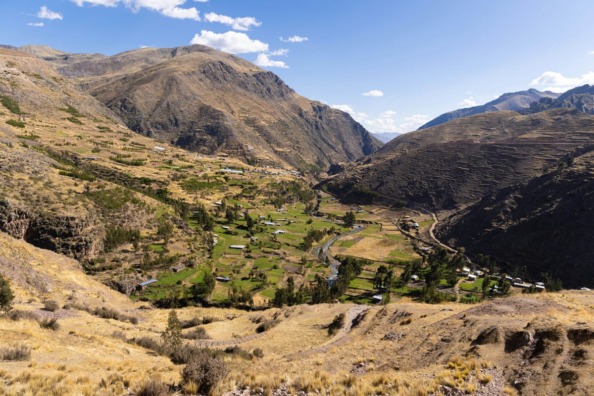 A green Andean valley of terraced fields between dry, rocky mountain slopes.