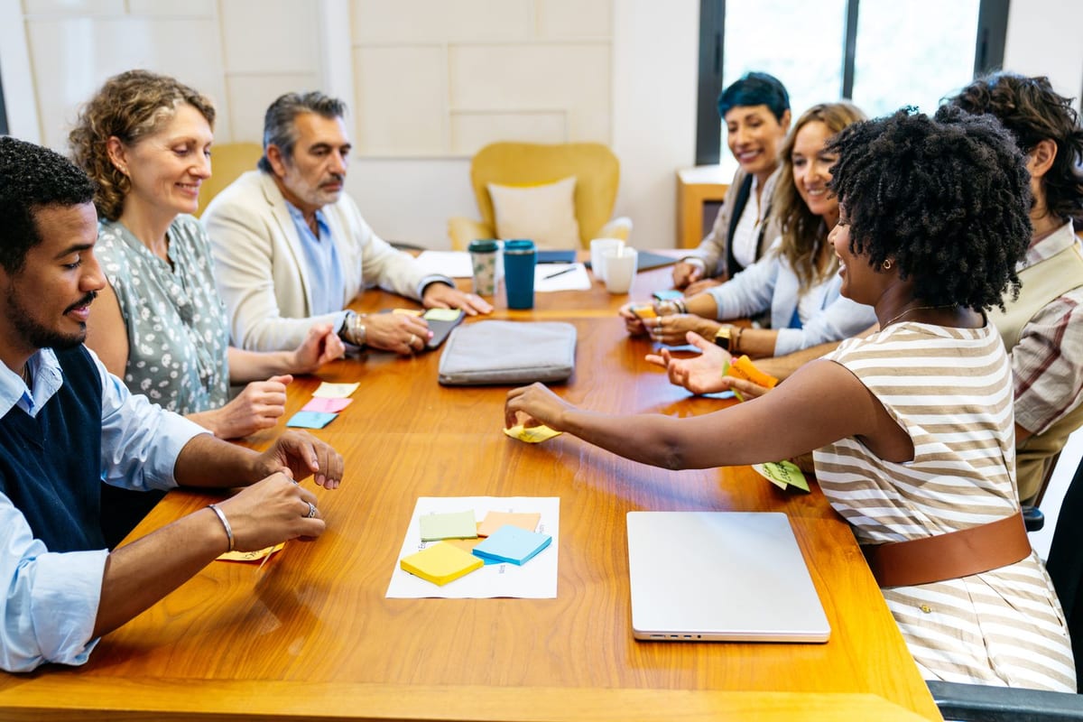 Colleagues around a wooden table, sorting colored sticky notes in a workshop.