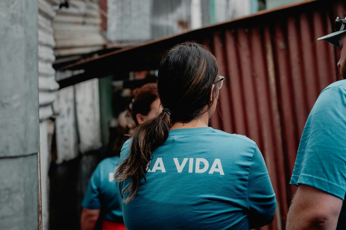 A team in matching shirts walking along a narrow passage between corrugated-metal homes.